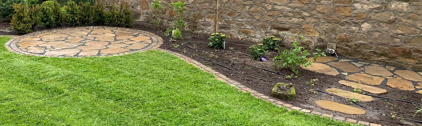 Gartenbeet mit Rasen, Natursteinmauer und Stauden