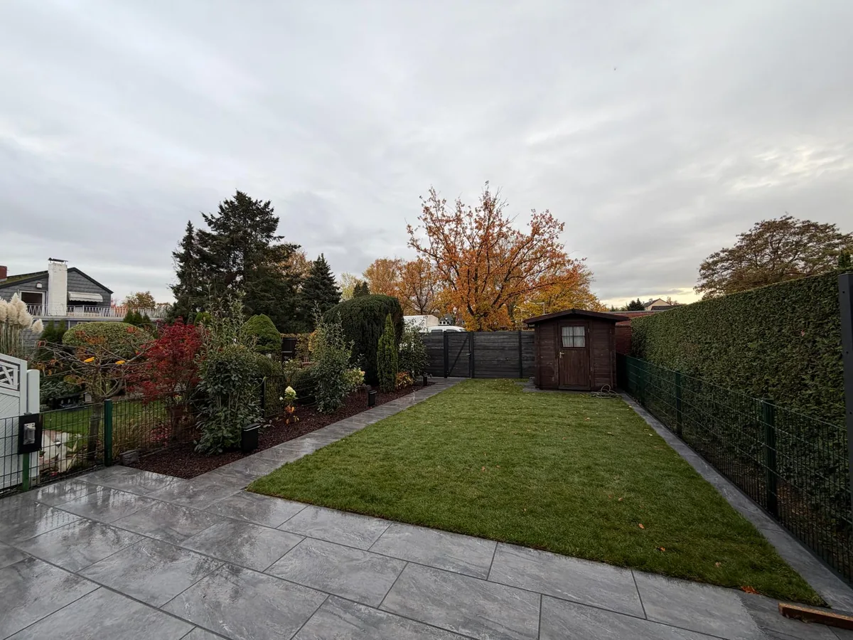 Terrasse aus großformatigen grauen Platten mit angrenzendem Rasen, Weg und Gartenhaus